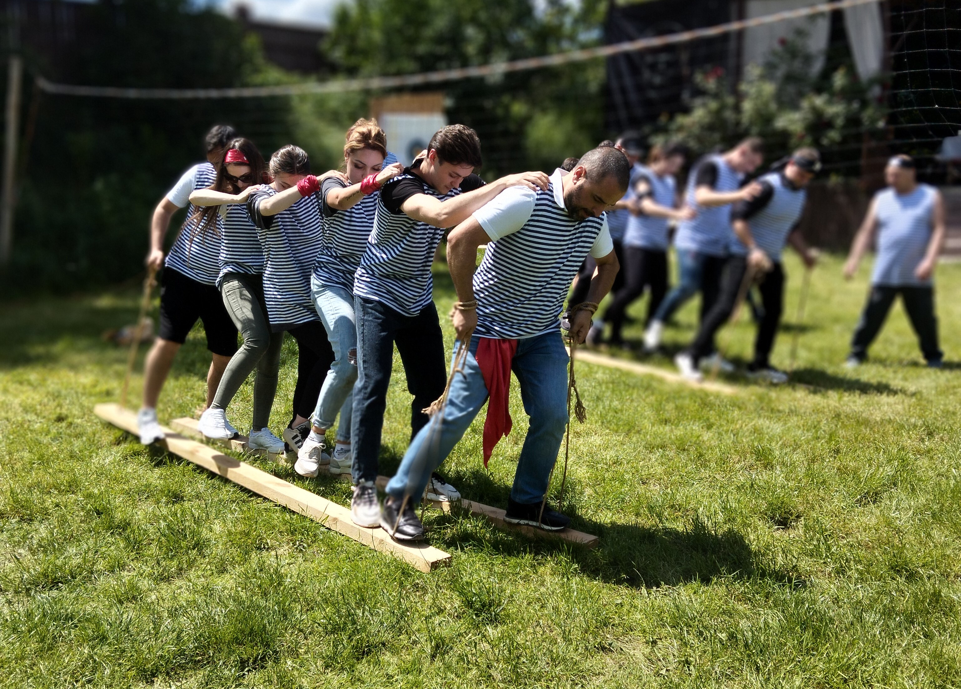 Echipă de angajați coordonându-se pe o placă de lemn în cadrul unei activități de teambuilding pentru echilibru și sincronizare